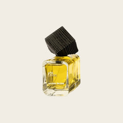 A small Maison Incense perfume bottle with a black ribbed cap, filled with yellow oil, set against a solid off-white background.